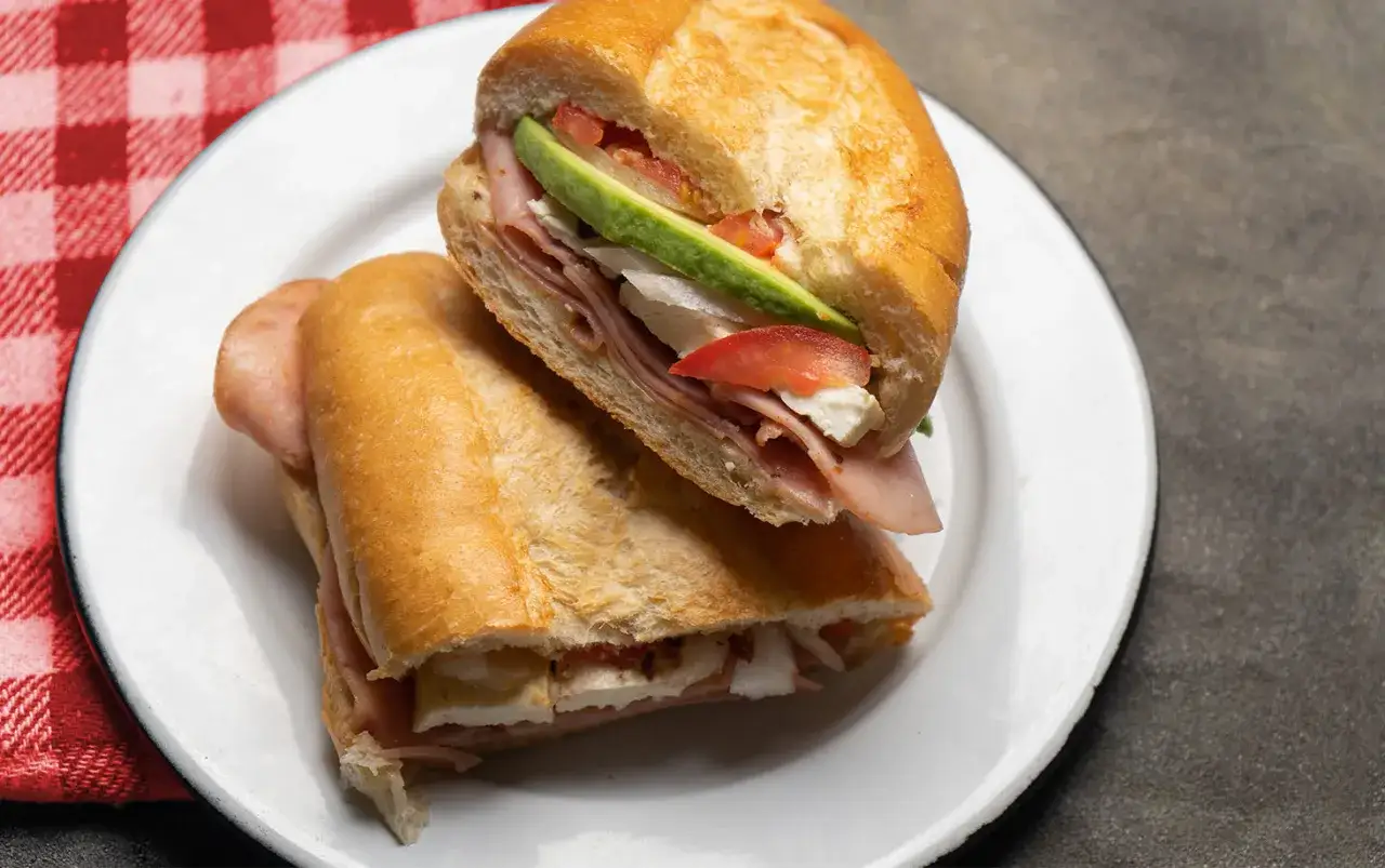 En saftig torta de jam&oacute;n med skinka, avokado, tomat och ost p&aring; ett rostat br&ouml;d.
