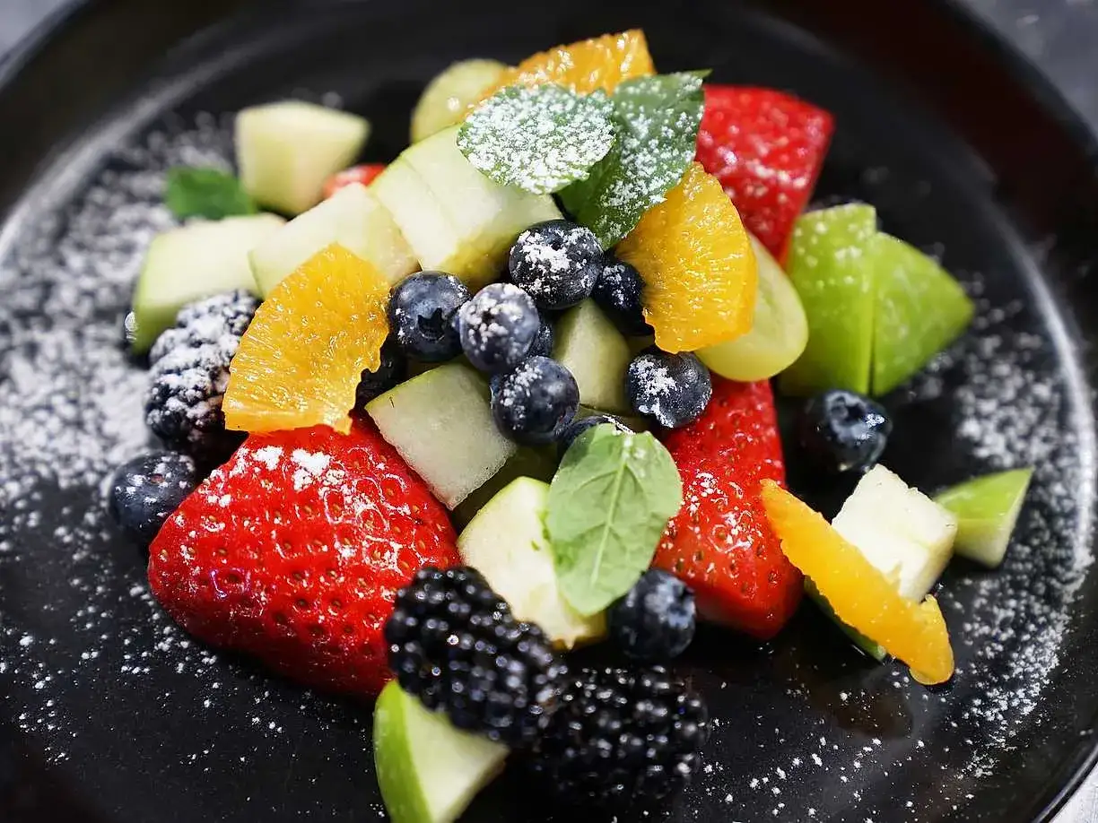 En f&auml;rgstark ensalada de frutas med jordgubbar, bl&aring;b&auml;r, bj&ouml;rnb&auml;r, &auml;pple och apelsin, pudrad med florsocker.