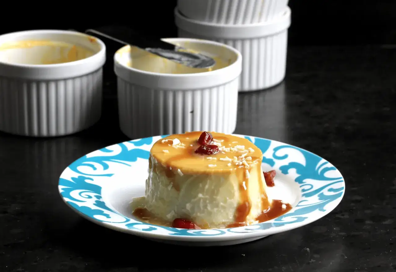 En krämig flan de coco med karamellsås och kokosflingor, serverad på en blåvit tallrik.