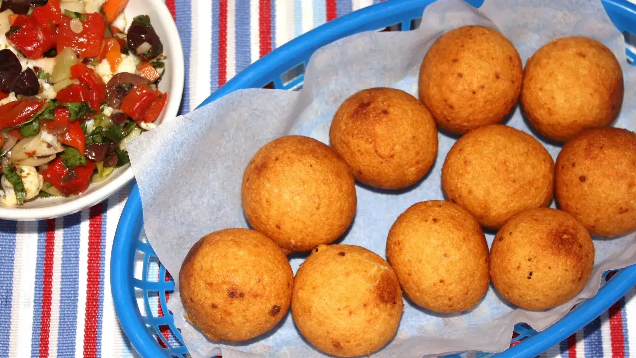 En korg med gyllene friterade bollar, som visar cómo hacer buñuelos. Bredvid en skål med en färgglad sallad.