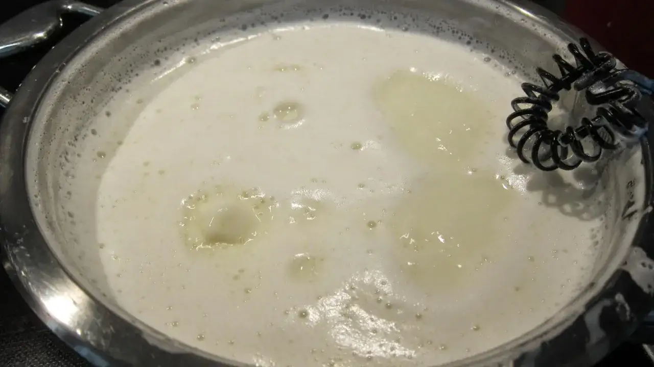 En kastrull med mjölk som bubblar, redo att bli arequipe. En visp ligger i.