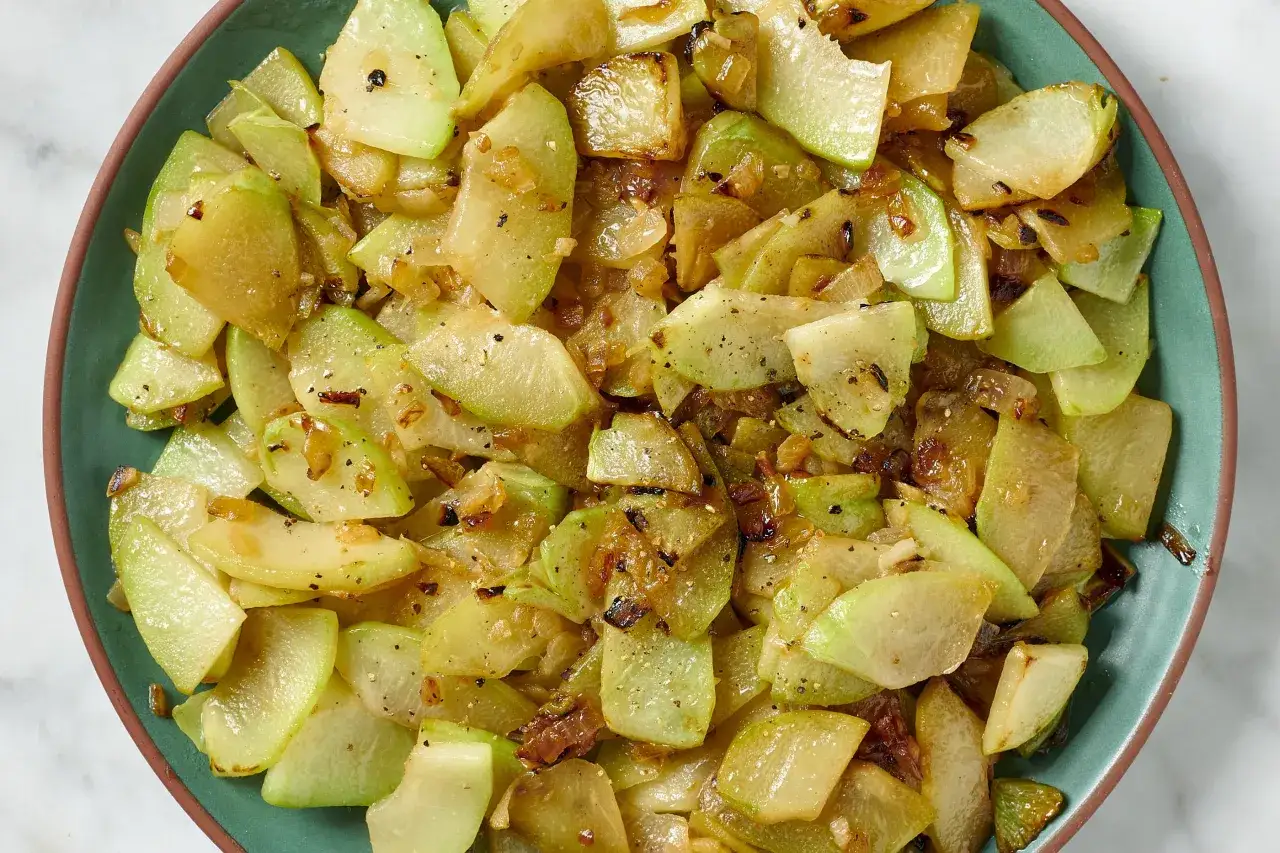 Stekt chayote, en mild grönsak, skuren i bitar och tillagad med lök och kryddor.