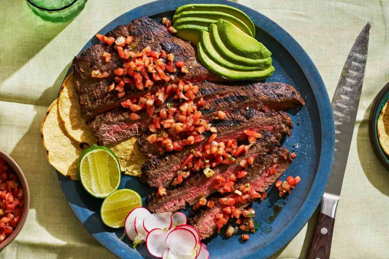 Saftig carne asada, skivad och toppad med pico de gallo, serveras med avokado, lime och rädisor på en blå tallrik.