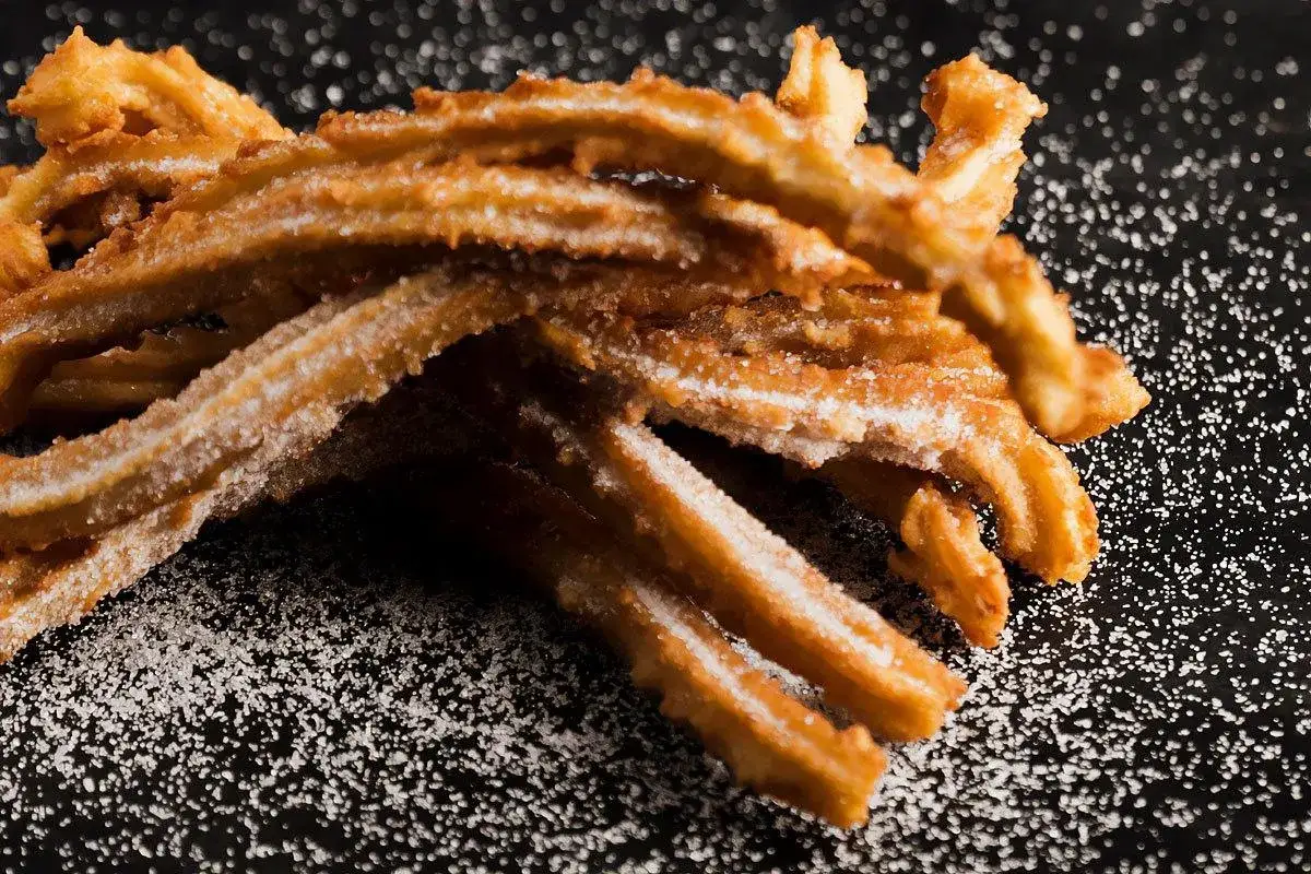 En hög med gyllene, sockerbeströdda churros españoles ligger på en mörk yta.