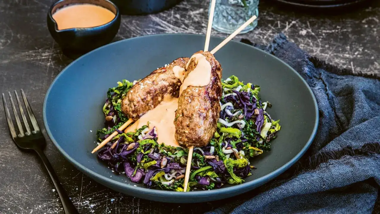 Två saftiga pinchos de carne med krämig sås, serverade på en bädd av färgglad kålsallad.