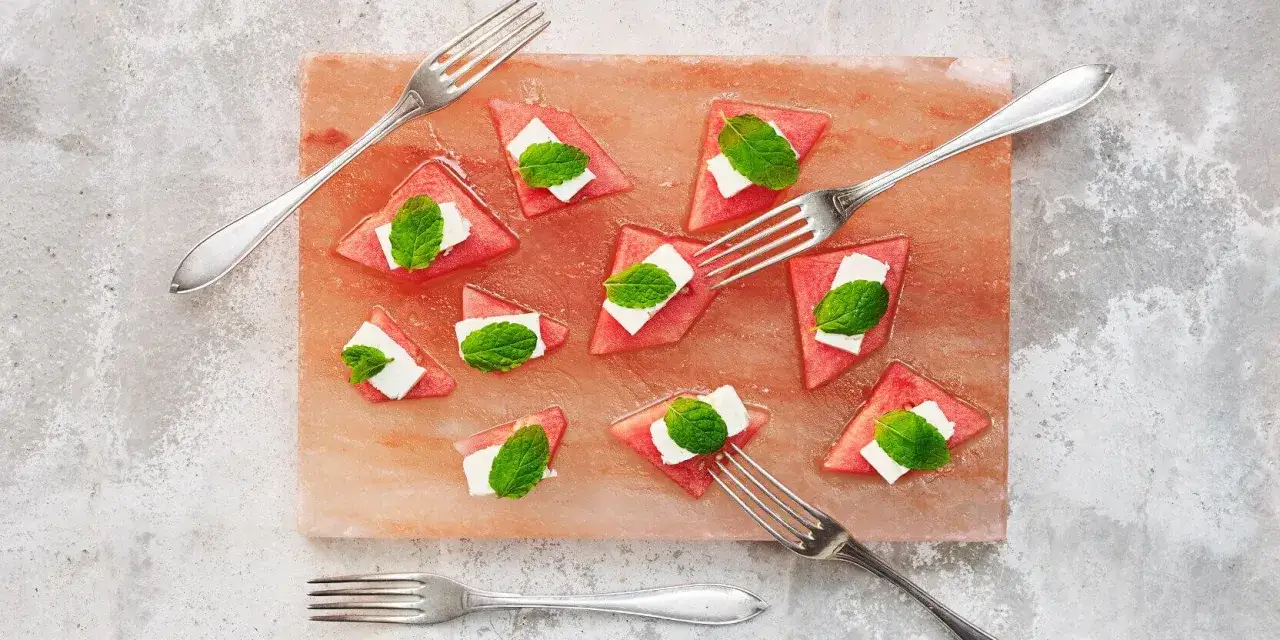 Vattenmelonbitar med fetaost och mynta p&aring; en rosa saltsten. En h&auml;rlig sommardessert, som en slags salmuera que es. Gafflar ligger utspridda.