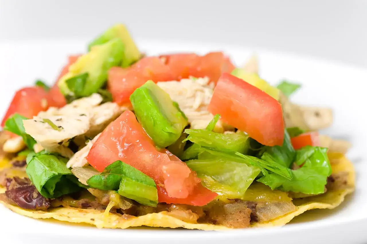 En n&auml;rbild p&aring; en l&auml;cker tostada de pollo med kyckling, tomat, avokado och sallad.