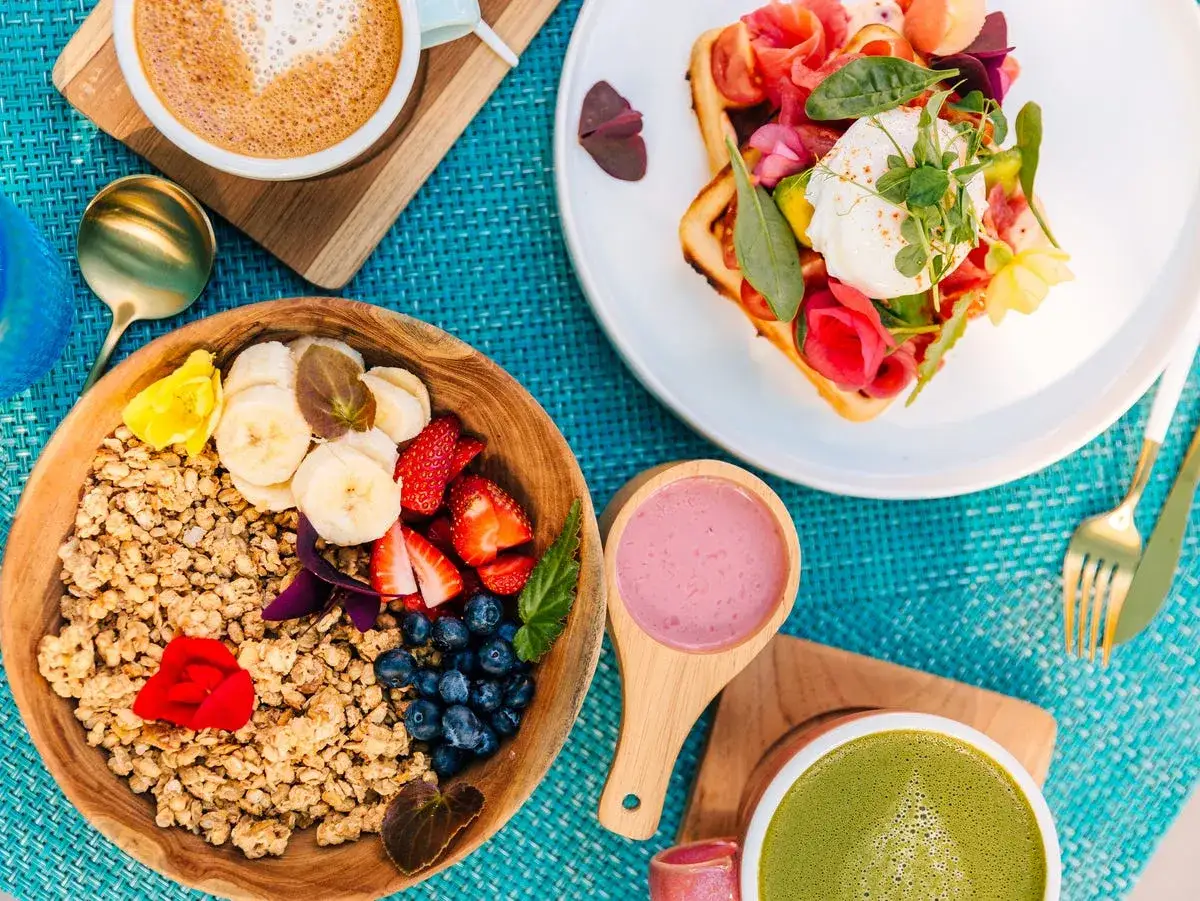 En härlig frukost med granola, bär, banan, en våffla med lax och pocherat ägg, samt kaffe och matcha. Perfekta desayunos saludables!