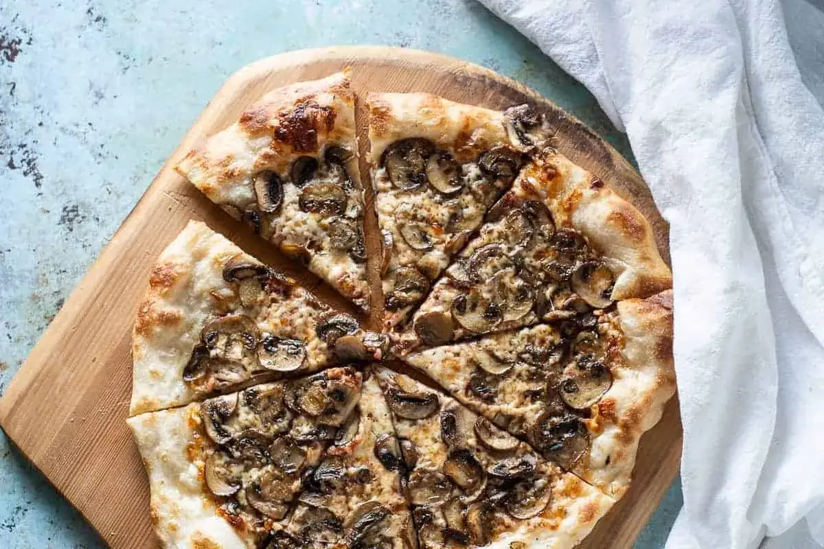 En skivad pizza de hongos med gyllene skorpa och rikligt med champinjoner, serverad på en träskärbräda.