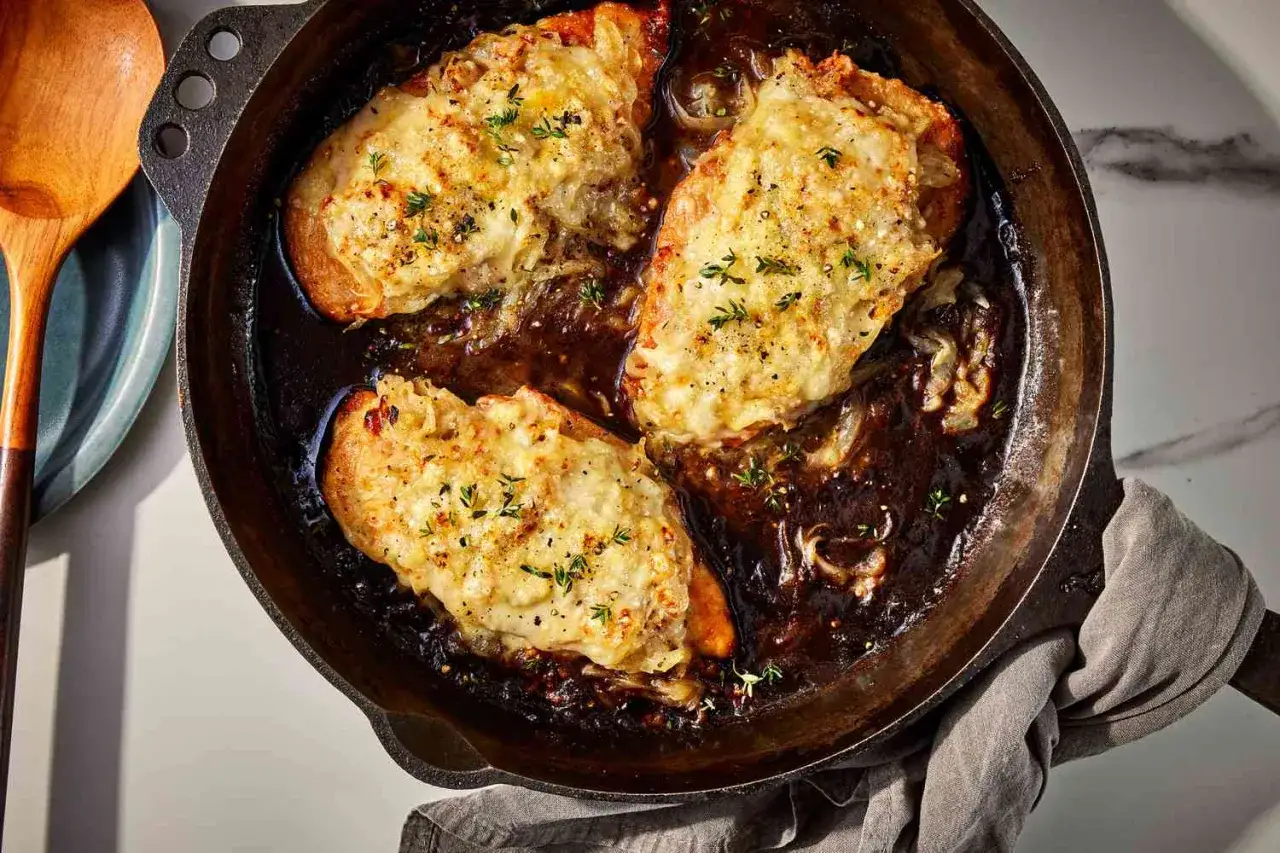Tre kycklingfiléer med smält ost och lök i en gjutjärnspanna. En härlig pollo encebollado som ser otroligt god ut.
