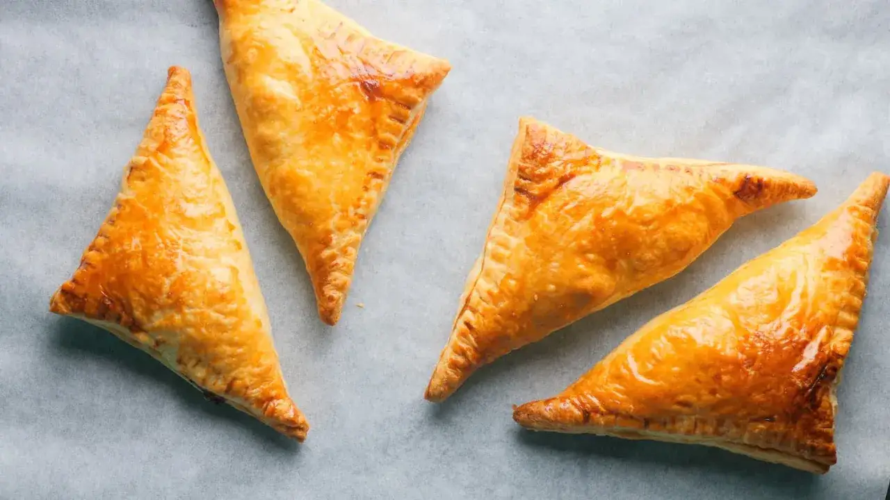 Gyldene, trekantede pastelitos de pollo ligger på bakepapir.