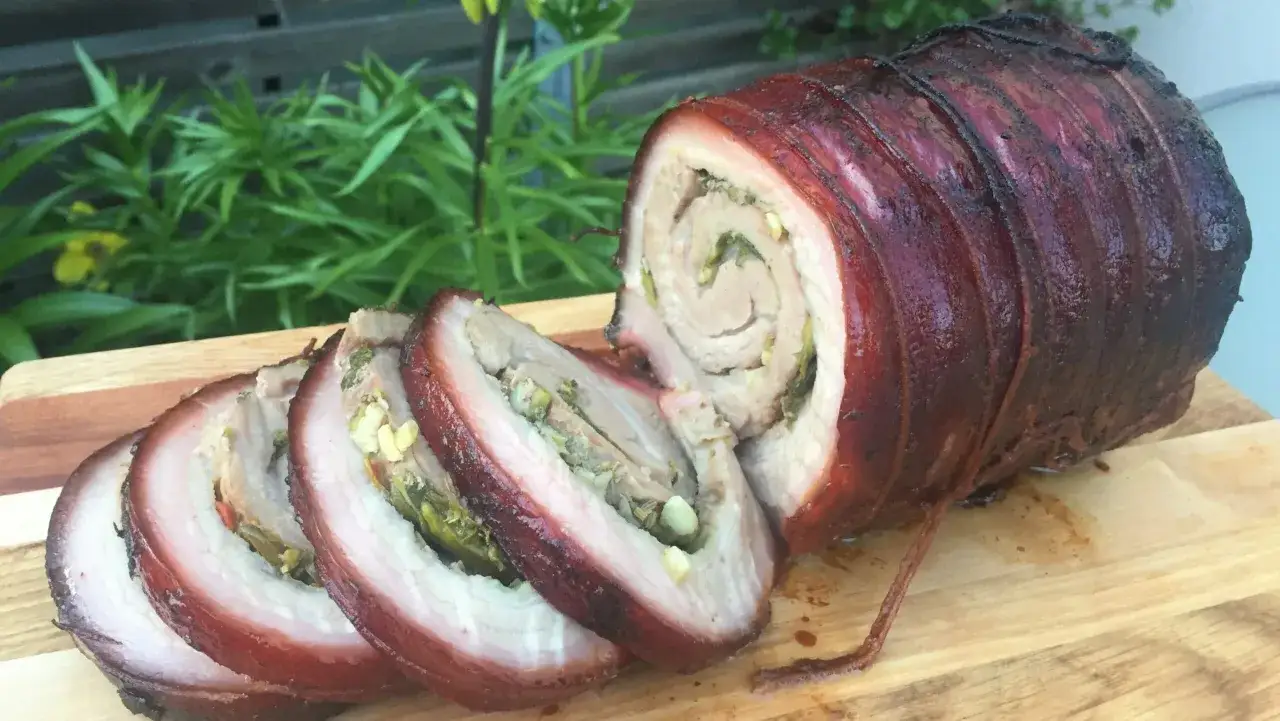 En saftig rullad fläskstek, carne de cerdo, med krispig svål och fyllning av örter. Skivorna visar den lockande insidan.