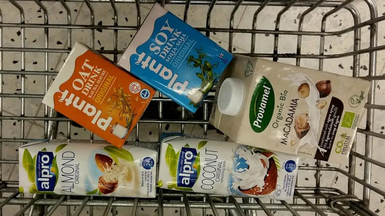 Olika tipos de leche i en kundvagn: havre, soja, mandel, kokos och makadamia.