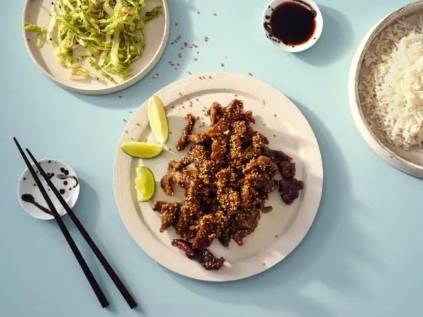 Krispiga chicharrones de cerdo med sesamfrön, serverade med ris, sallad och limeklyftor.