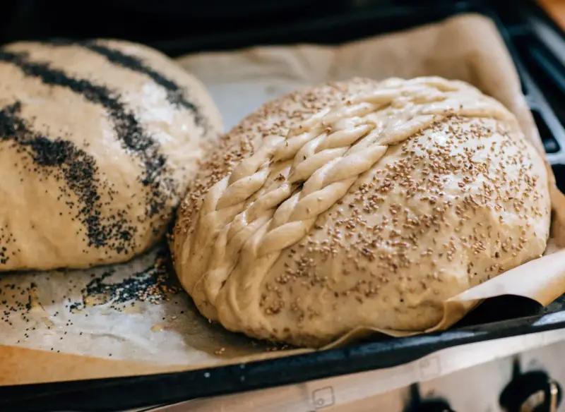 Två olika tipos de pan dulce, en med vallmofrön och en flätad med sesamfrön, redo att bakas.