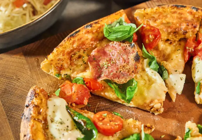 Njut av en utsökt pizza med färska **ingredientes para pizza** som salami, tomater och basilika, serverad på en träskärbräda.