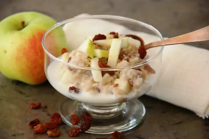 En skål med havregrynsgröt med äppelbitar och russin, bredvid ett äpple. Enkel guide för como preparar avena.
