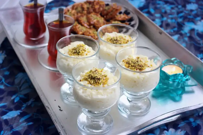 Fyra glas med krämig arroz en leche salvadoreño, toppad med pistagenötter. Två glas med te och en ljuslykta fulländar serveringen.
